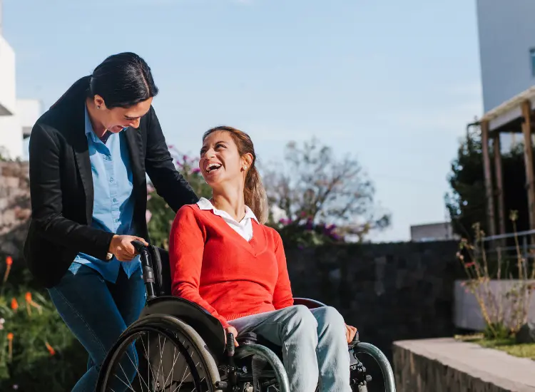 Disabled woman in wheelchair smiling and looking up at support worker